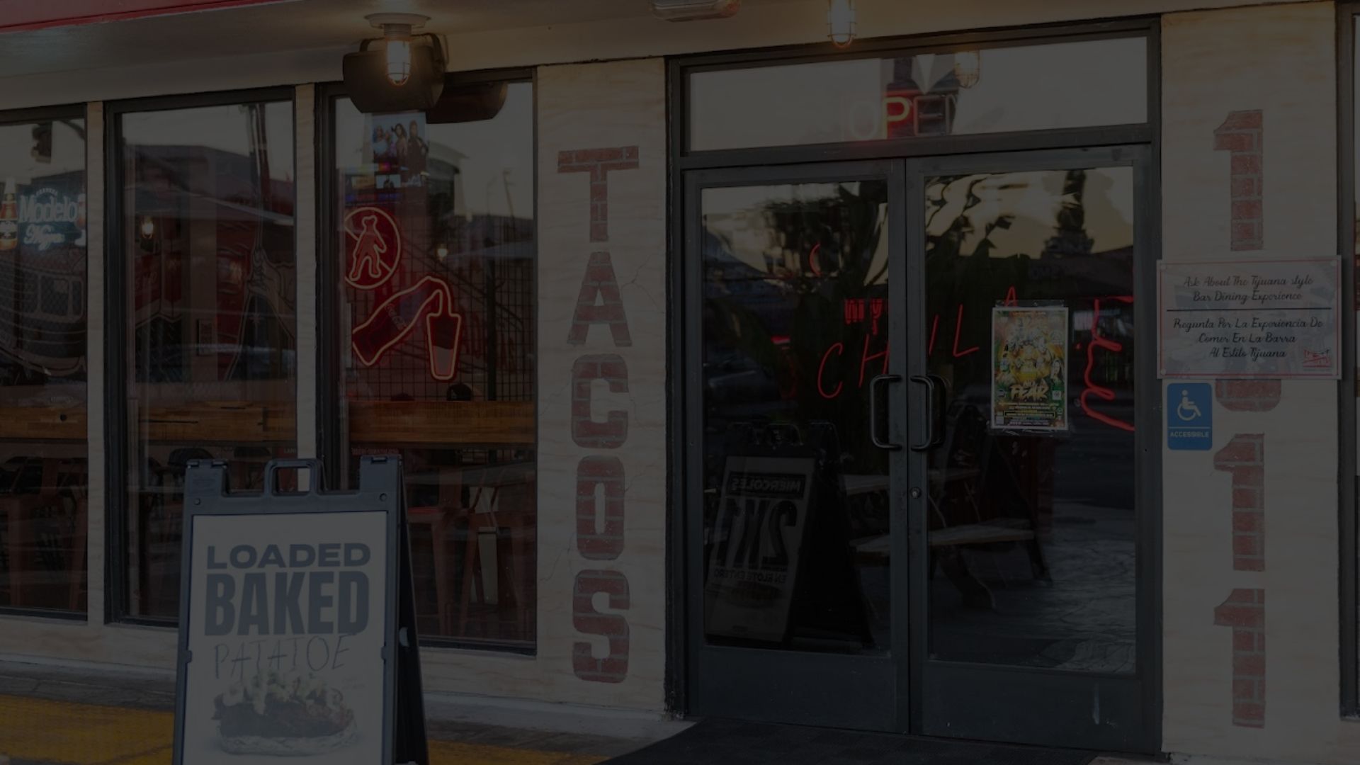 Las Ahumaderas storefront at night: TACOS painted on the brick, neon signs glowing, the number 1011 by the door
